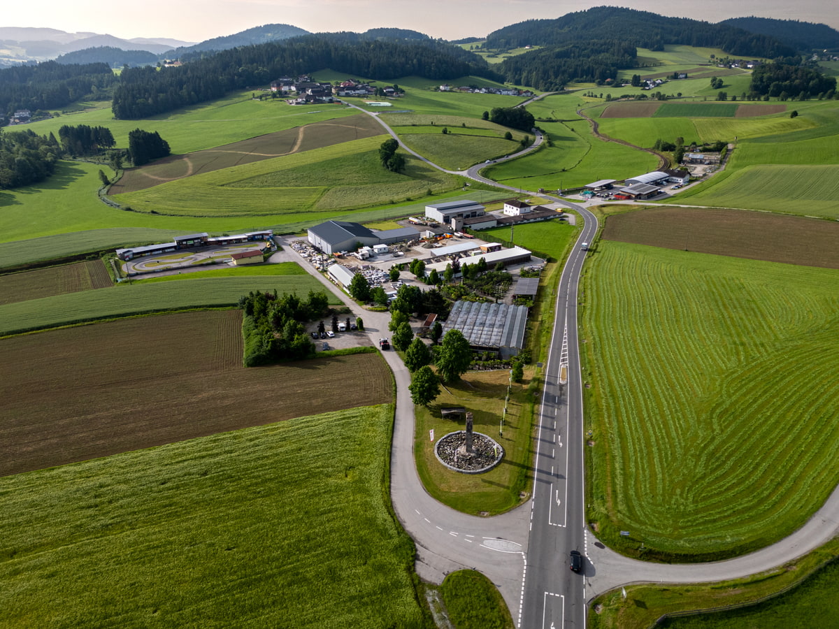 Luftaufnahme Gartencenter mit Gebäuden, Gewächshäusern, grünen Feldern und bewaldeten Hügeln