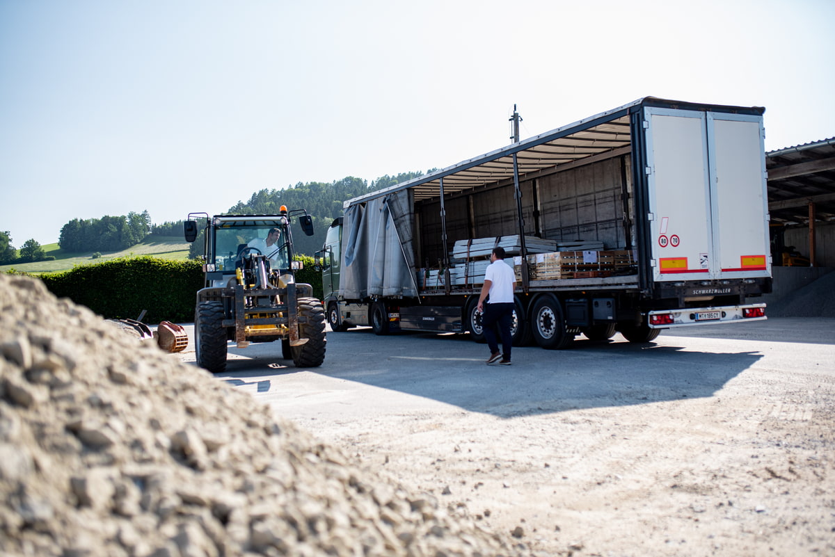 LKW wird beladen, Gabelstapler im Vordergrund, Mitarbeiter koordinieren Lieferung vor Gebäude