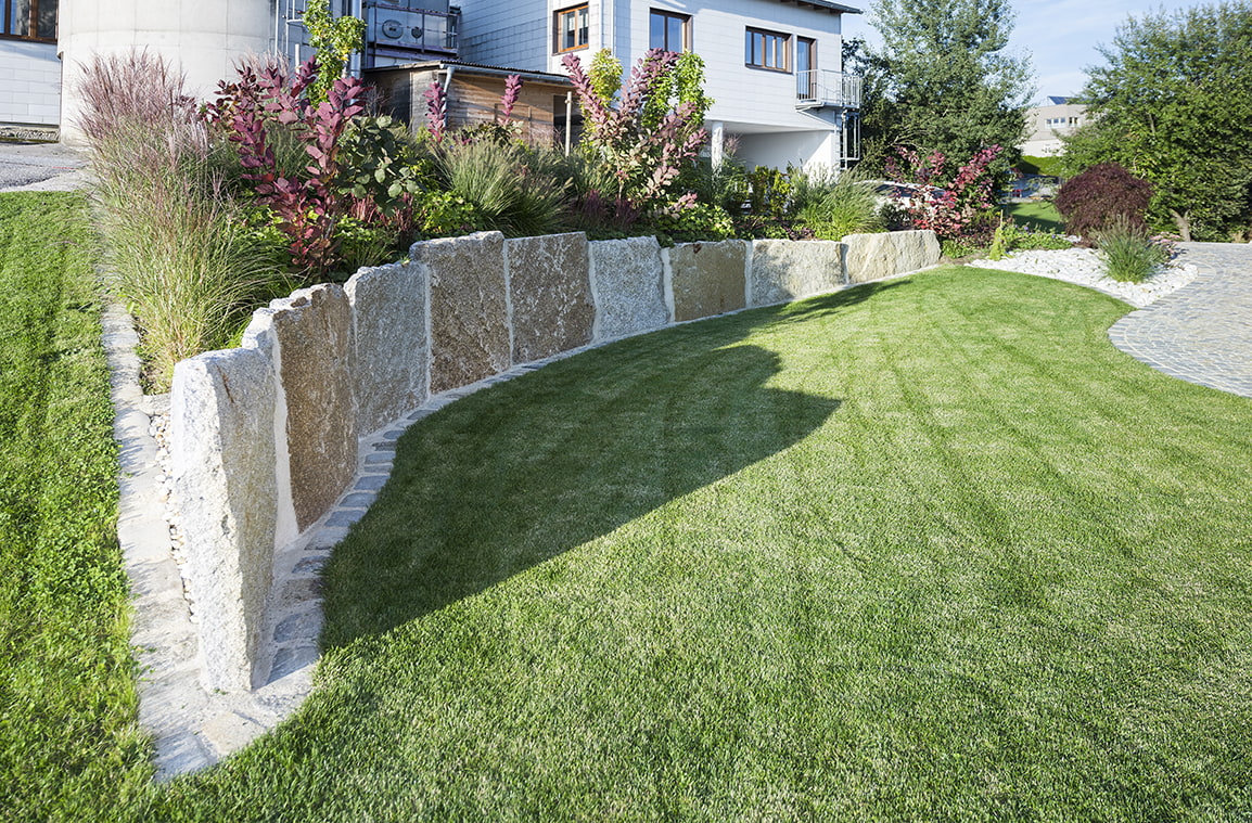 Moderne Trockenmauer aus Krustenplatten mit Rasen und Beeten