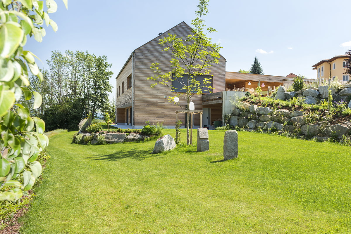 Apfelblüten links vorne, Rasen, junge Bäume, Findlinge, modernes Holzhaus hinten Apfelblüten links vorne, Rasen, junge Bäume, Findlinge, modernes Holzhaus hinten